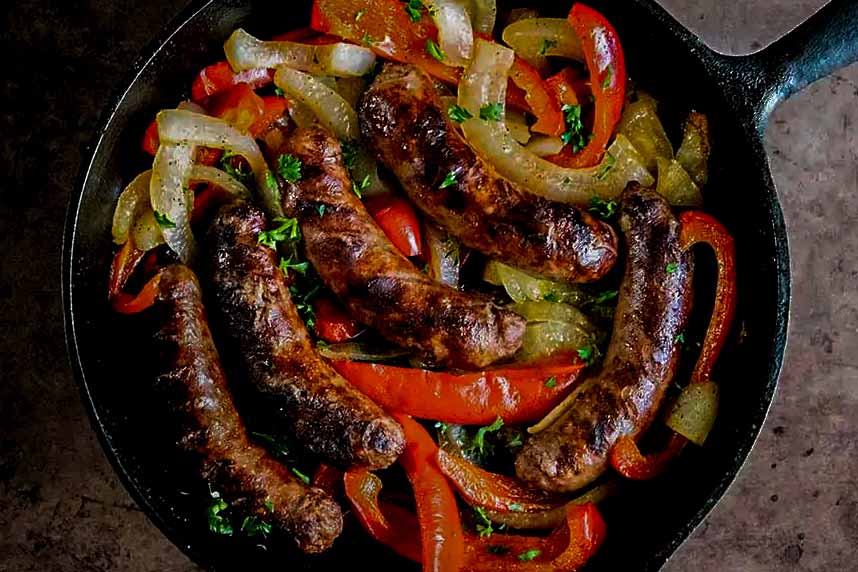 Beer brats in peppers and onions in a cast iron skillet